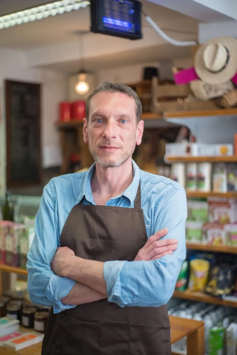 aged, apron, arms, arms crossed, business, commercial, company, confidently, corporate, crossed, deli, enterprise, grocery, his, middle, office, owner, portrait, professional, shelves, shop owner, shopkeeper, small, small business, standing, store